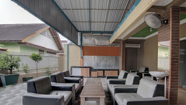 A covered outdoor seating area with sofas and a table, a kitchen area with cabinets, and a brick wall. - OYO 92833 Penginapan Syariah (Pekanbaru)