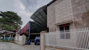 A building with a covered parking area, a white fence, and a blue car parked inside. - OYO 92833 Penginapan Syariah (Pekanbaru)