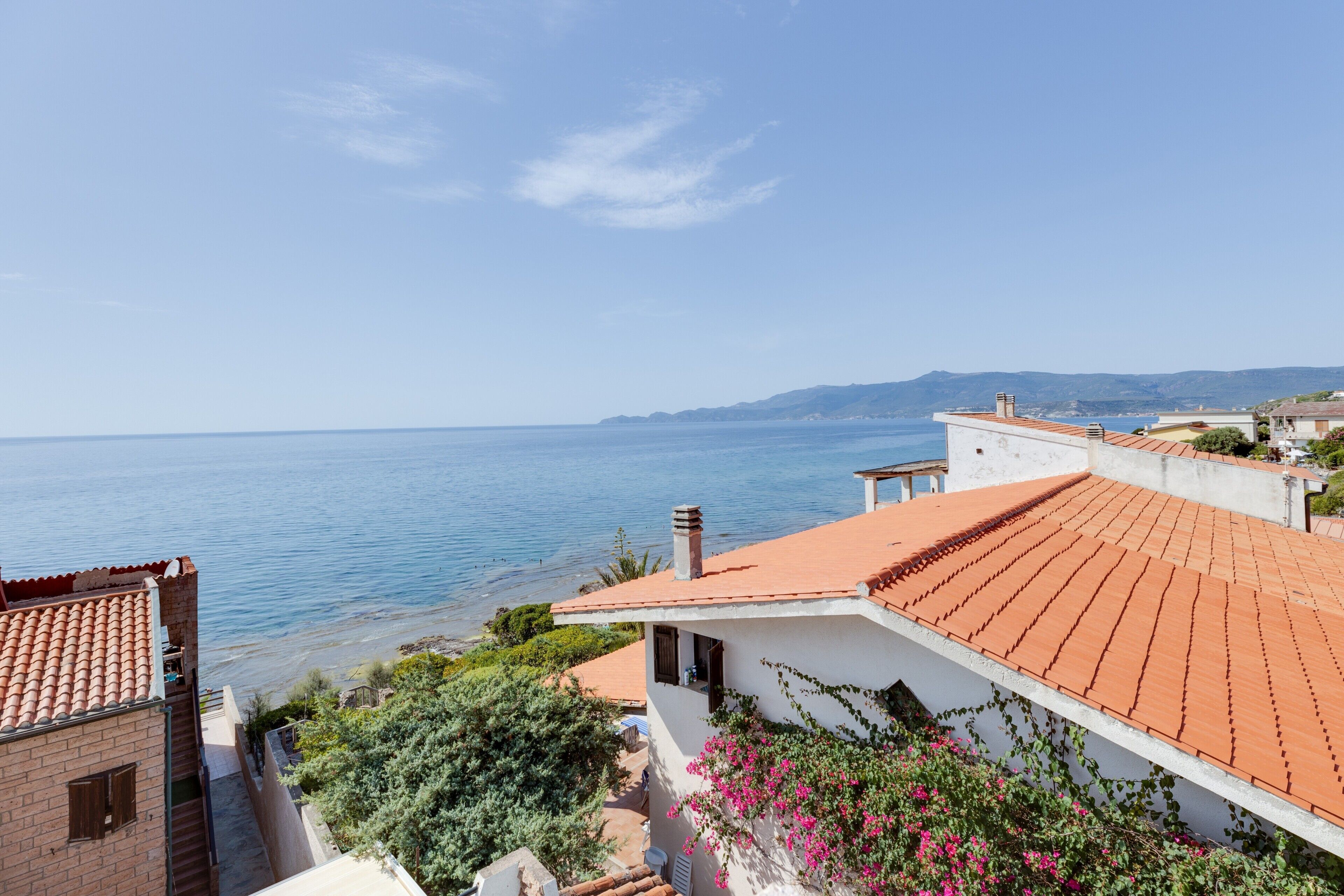 Un bâtiment situé sur la côte, avec un toit recouvert de tuiles rouges, un balcon et une vue sur la mer.