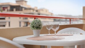 Un balcon avec une petite table, deux verres à vin et une plante en pot.