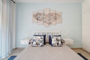 Une chambre à coucher comprenant un lit, deux tables de chevet, une œuvre d’art murale et un rideau.