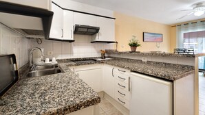 Une cuisine dotée de plans de travail en granit, de meubles blancs, d’un four encastré et d’un four à micro-ondes.