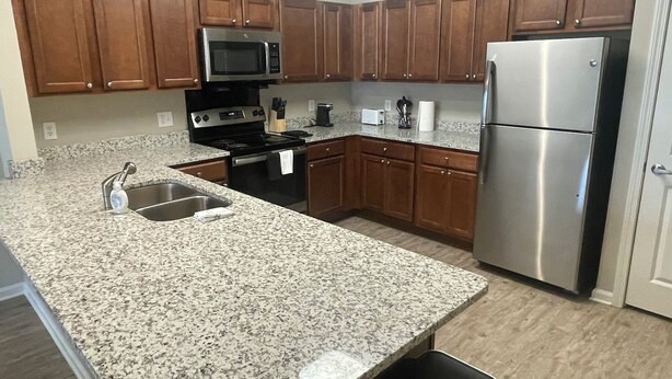 Una cocina con encimeras de granito, armarios de madera y electrodomésticos de acero inoxidable, además de un cubo de basura negro.