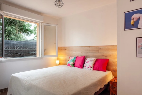 A bedroom with a bed, a window, a nightstand, and a wall-mounted lamp.
