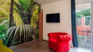 Una habitación con un amplio mural tropical, un sofá rojo, un televisor de pantalla plana y un ventanal corredero que da a un espacio exterior.