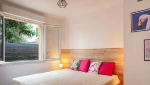 Un dormitorio con cama, ventana, mesita de noche y una lámpara de pared.
