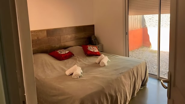 Ein Schlafzimmer mit einem Bett, Kissen, einer Kopfteil, einer Tür und Blick durch eine Glastür.
