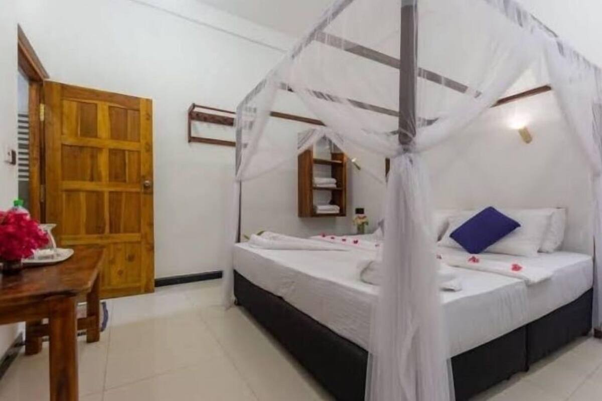 Una habitación con cama bajo un dosel, una puerta de madera y una mesita con un florero.