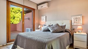 A bedroom with a bed, nightstands, a wall-mounted air conditioner, and a sliding glass door leading to an outdoor area.