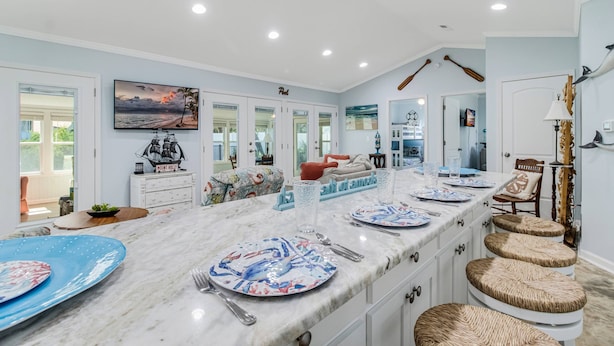 A spacious kitchen with a long island, white cabinets, and a dining area with stools. - Updated Beach Cottage with Wonderful Pool Near Beach Access (Oak Island)