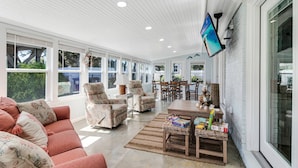 A spacious sunroom with a large window, a wooden ceiling, and a flat-screen TV mounted on the wall. - Updated Beach Cottage with Wonderful Pool Near Beach Access (Oak Island)
