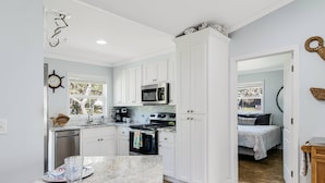A compact kitchen with white cabinets, a microwave, and a stove. A dining area with a table and chairs is visible. - Updated Beach Cottage with Wonderful Pool Near Beach Access (Oak Island)