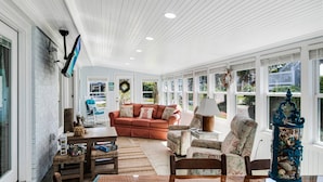 A spacious living room with a large window, a fireplace, and a dining area with a table and chairs. - Updated Beach Cottage with Wonderful Pool Near Beach Access (Oak Island)