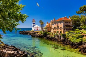 Un edificio costero con un faro, mar azul cristalino y una costa rocosa.