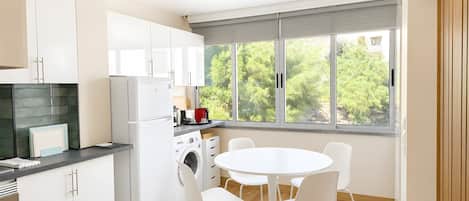 Una cocina moderna con armarios blancos, lavadora integrada y un comedor con mesa y sillas redondas.
