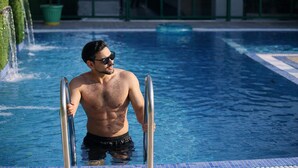 A man in black swim trunks stepping out of a pool with a clear blue sky and a building in the background. - The Prominence Hotel (Dehradun)