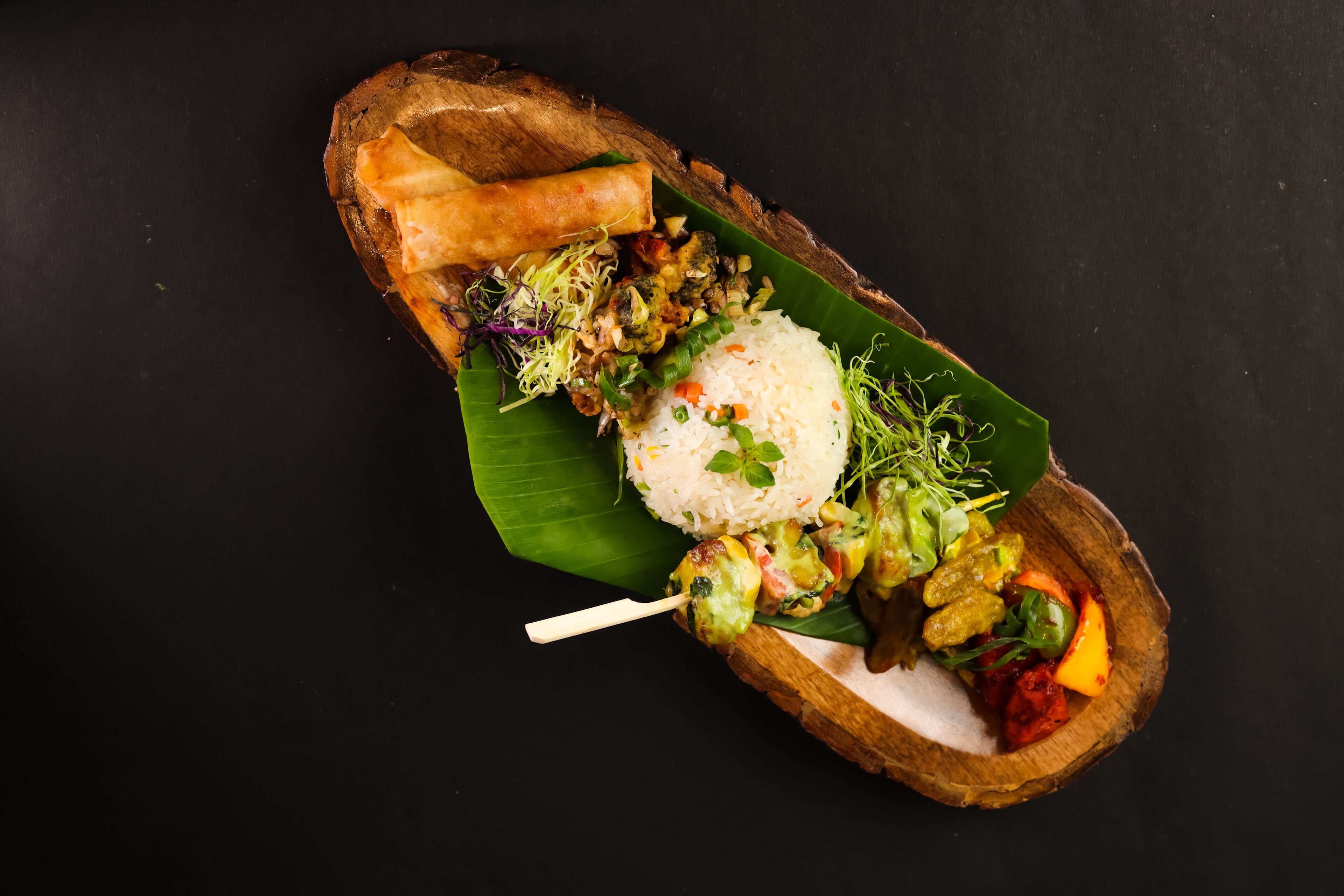 A meal served on a banana leaf with rice, vegetables, and a spring roll.