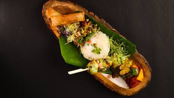A meal served on a banana leaf with rice, vegetables, and a spring roll.