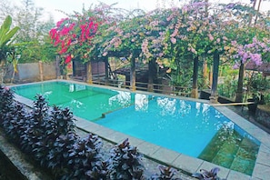 Ein rechteckiger Pool mit Holzterrasse und einer Pergola, die mit blühenden Weinreben bewachsen ist.