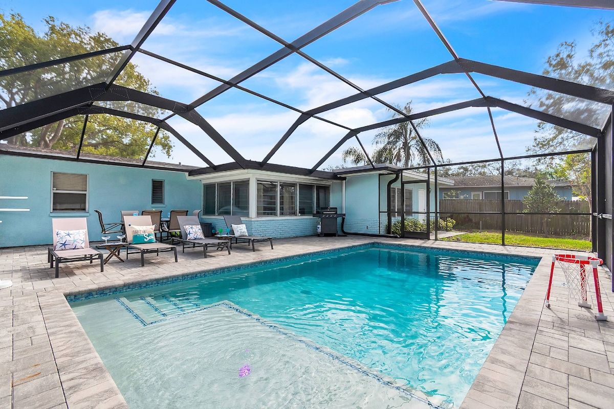 A swimming pool with a covered area, lounge chairs, and a view of the backyard.
