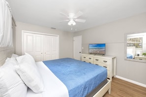 Een slaapkamer met een bed, een plafondventilator, een televisie, een dressoir en een raam.