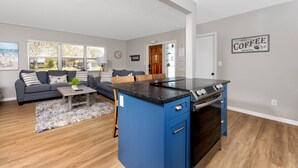 A modern kitchen with a blue island, a dining area with a sofa, and a view of the outdoors. - Close to Beach! Heated Pool! Pets OK! Private/Fenced-in Backyard! Rock to Beach Home ~ Largo, FL (Largo)