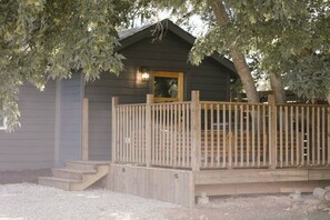 A wooden cabin with a porch and a door, surrounded by trees.