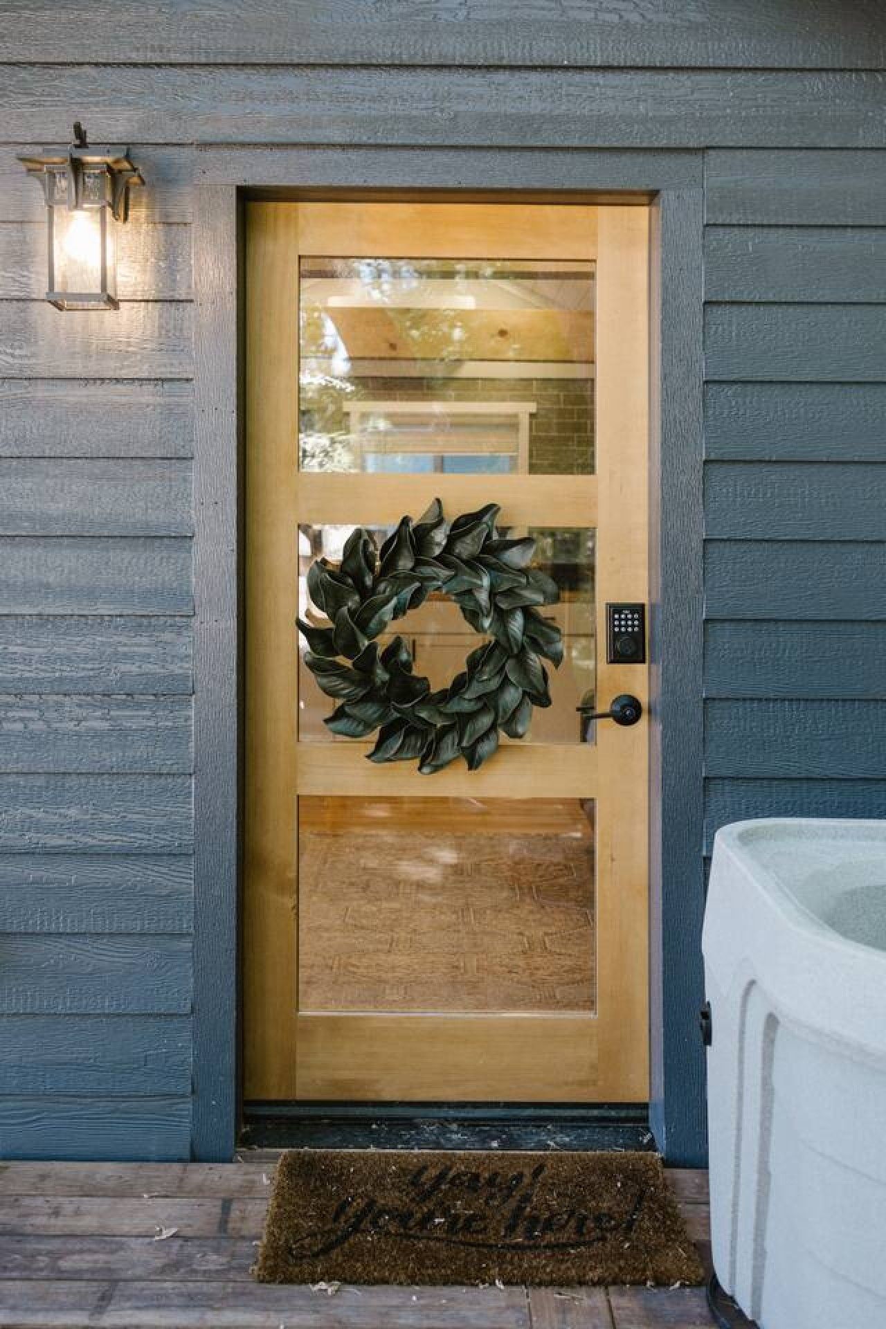 Une porte en bois ornée d’une guirlande, dotée d’un clavier pour ouvrir la serrure et surmontée d’un paillasson.