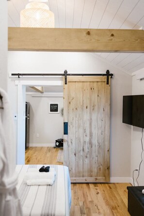 A bedroom with a bed, a sliding door, a television, and a hallway leading to a bathroom.