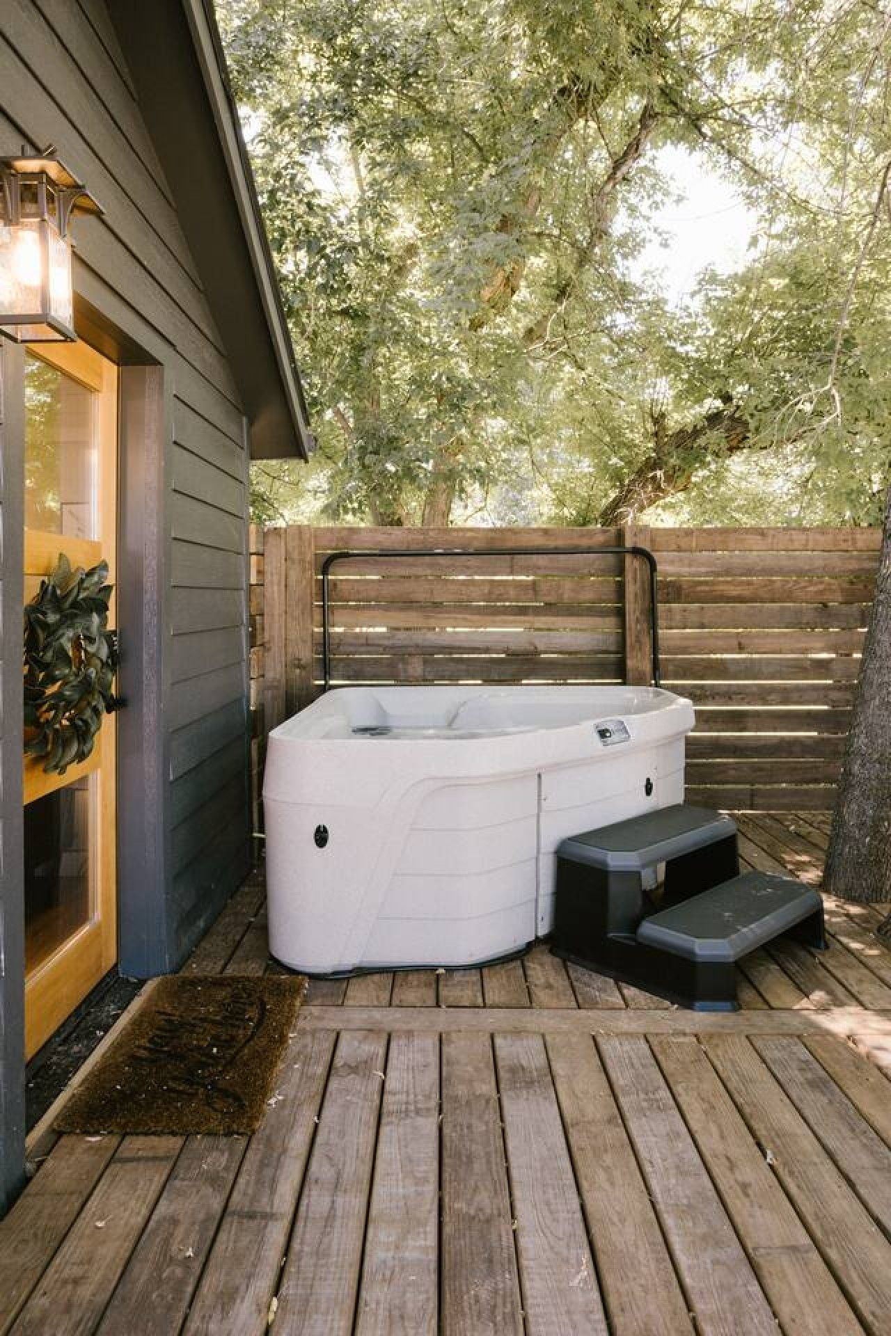 Un bain à remous sur une terrasse en bois, avec une clôture en bois et des arbres en arrière-plan.