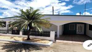 Um edifício moderno com fachada branca, cerca preta e uma palmeira em primeiro plano.