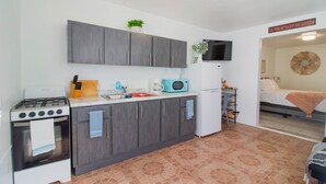 Uma cozinha compacta com armários cinzentos, fogão branco e micro-ondas azul.