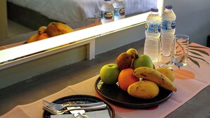 A hotel room with a bed, a table with fruit and drinks, and a window with curtains. - Maiiam Bungalows (Karon)