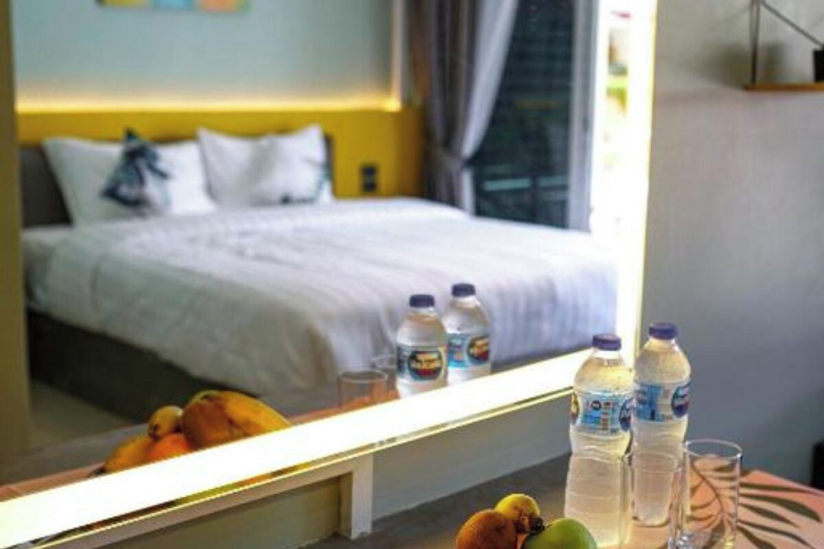 A hotel room with a bed, a mirror reflecting the room, a table with water bottles and a glass, and a window with curtains.