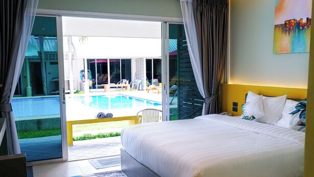 A hotel room with a large bed, a view of a swimming pool, and a sliding glass door leading to an outdoor area. - Maiiam Bungalows (Karon)