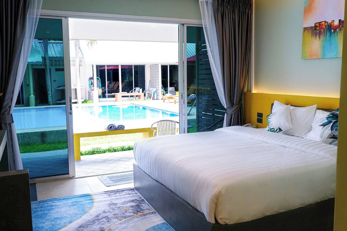 A hotel room with a large bed, a view of a swimming pool, and a sliding glass door leading to an outdoor area.
