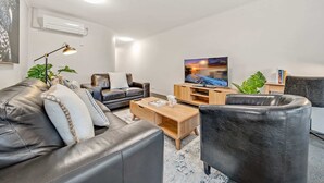 Una sala de estar moderna con sofás de cuero, una mesa de centro de madera y un televisor de pantalla plana sobre un mueble de madera.