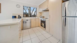 Una cocina moderna con armarios de madera, un refrigerador de acero inoxidable, un lavavajillas, un horno y una ventana con vistas a árboles.
