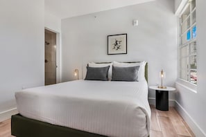 Relax in a serene space with a large bed, side table, and artwork above, offering a view of the outside.