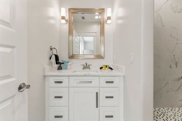 A bathroom with a white vanity, a mirror with a gold frame, and marble-patterned walls.