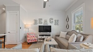 A living room with a television, a sofa, a chair, and a wall with the word "BEACH" spelled out.