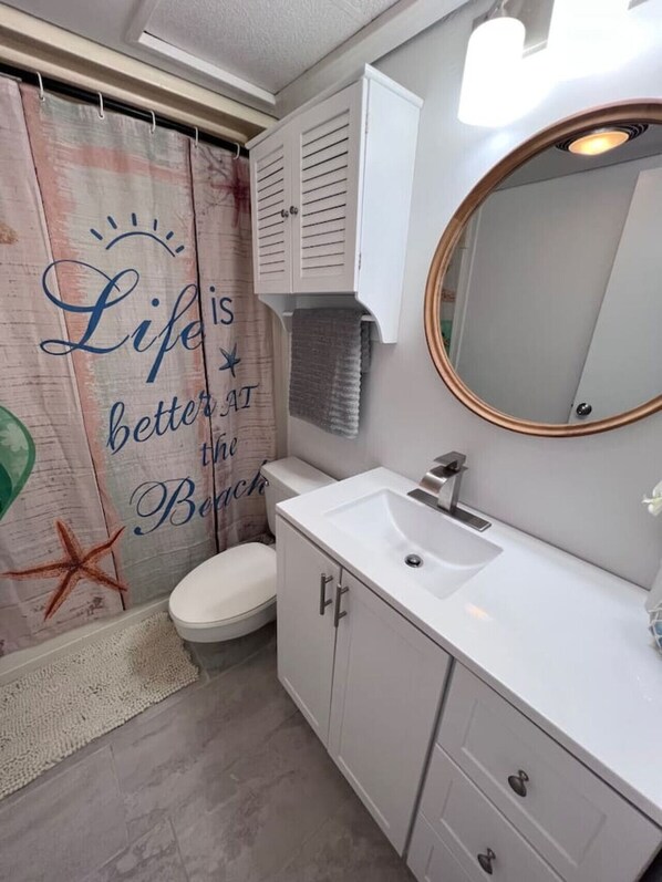 A bathroom with a shower curtain featuring a beach theme, a white sink, a mirror, and a cabinet. - Destin Condo|Walk to Beach|Community Pool & Hot Tub (Destin)