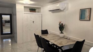 Zona pranzo con tavolo in marmo, sedie nere, una pianta in vaso e condizionatore a muro.