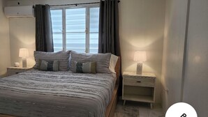 Una camera da letto con un letto, due comodini, una finestra con tende e un condizionatore.