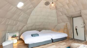 Een gezellige tentkamer met een bed, een tafeltje met een lamp, en een ladder tegen de muur.