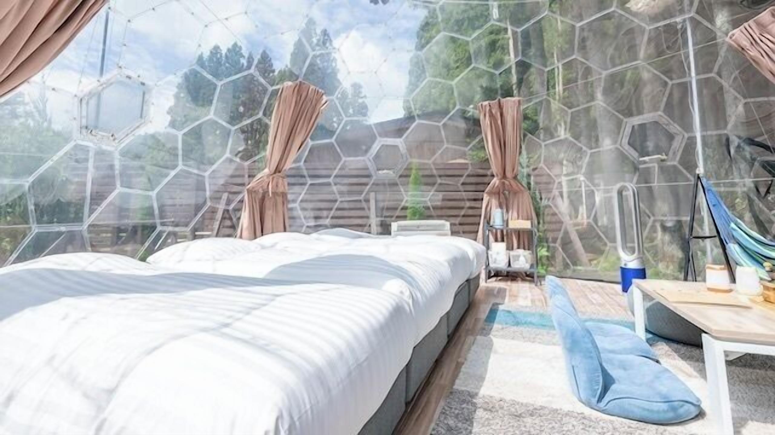 A room with a bed, a table, a hammock, and a view through a hexagonal window.