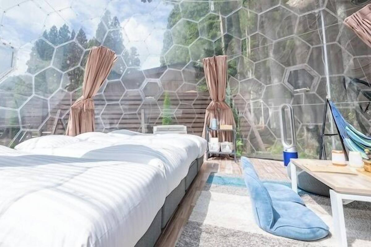 A room with a bed, a table, a hammock, and a view through a hexagonal window.