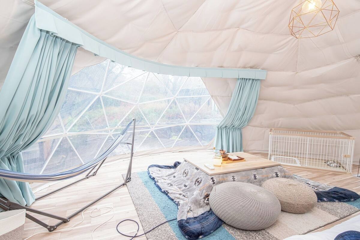 A tented room with a hammock, a crib, and a view of the outdoors.