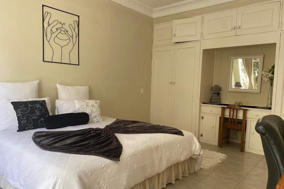 Une chambre à coucher avec un lit, des murs blancs, une œuvre d’art encadrée, un bureau et une chaise.