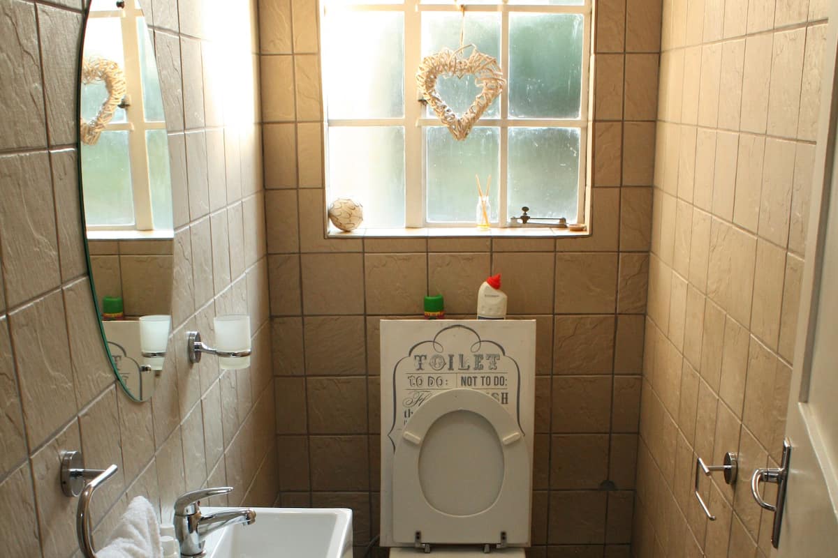 Une salle de bain avec un lavabo, des toilettes et une fenêtre ornée d’un motif en forme de cœur.